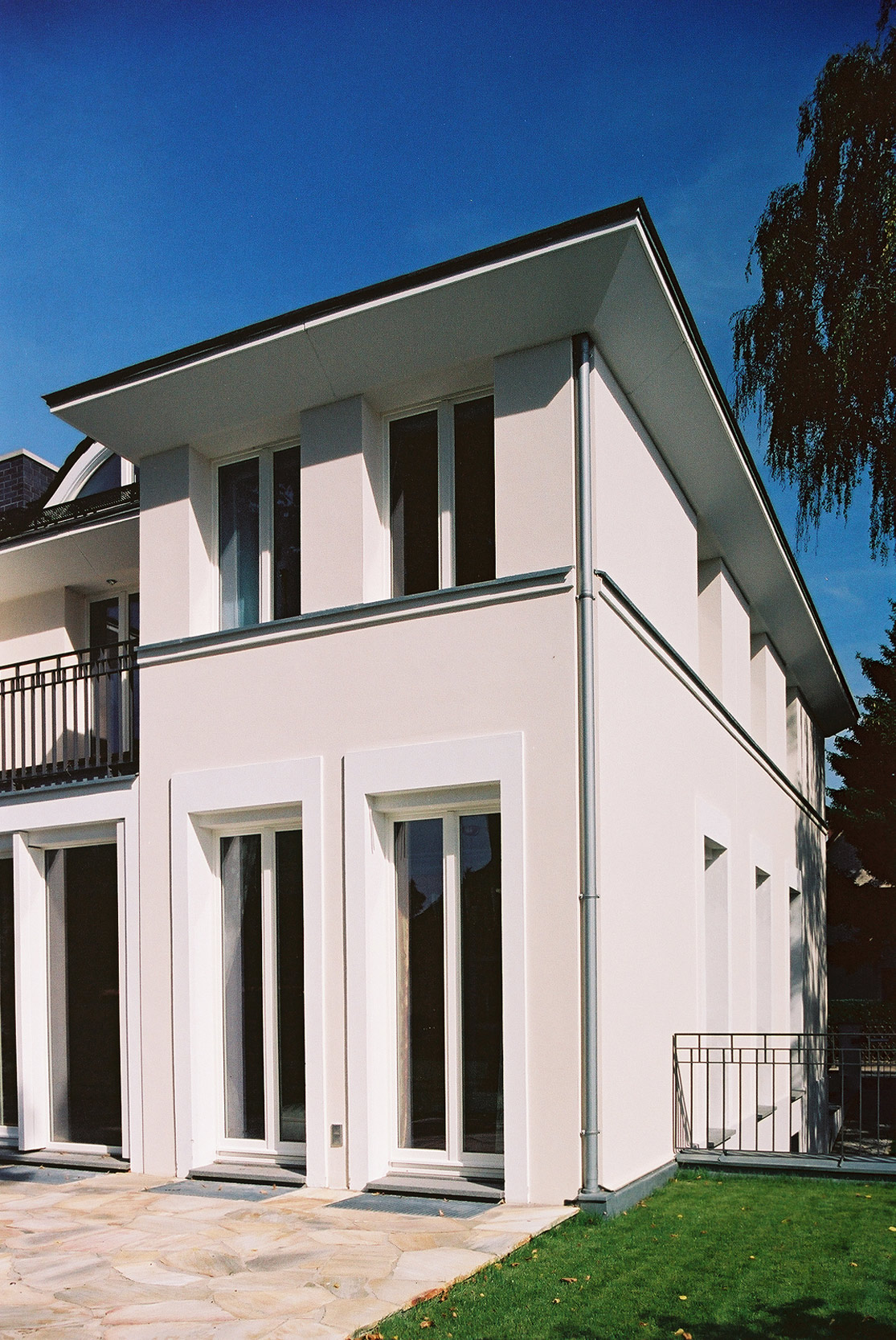 Französische Fenster und eine weit auskragende Attika vergfeinnern die Fassade des Hauses.
